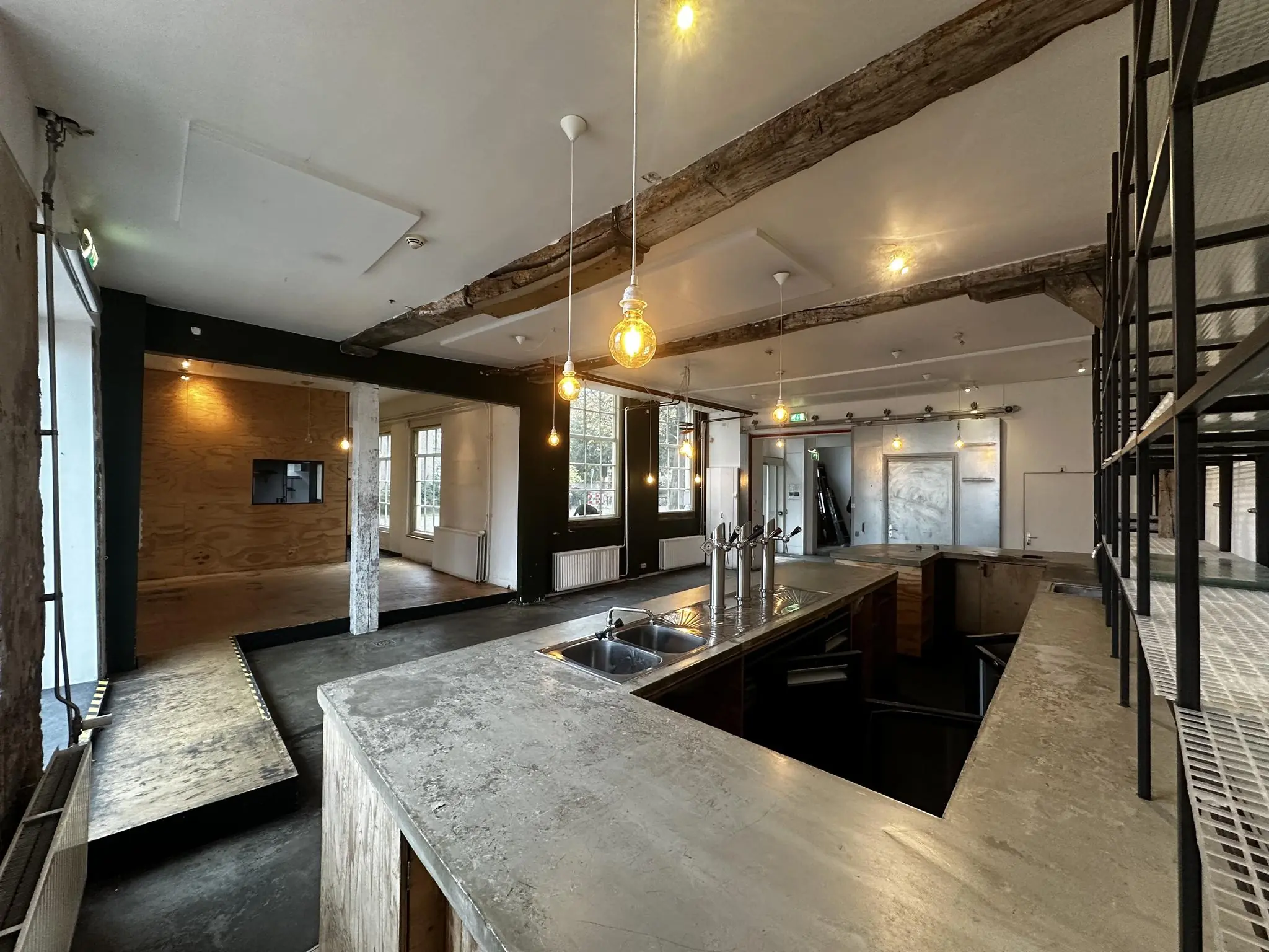 Moderne horecaruimte aan het Sint-Agathaplein met betonnen bar, industriële details en zichtbare houten balken.